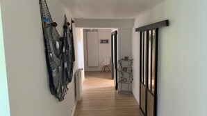 A hallway with a wooden floor, a white chair, and a wall-mounted shelf with pictures.