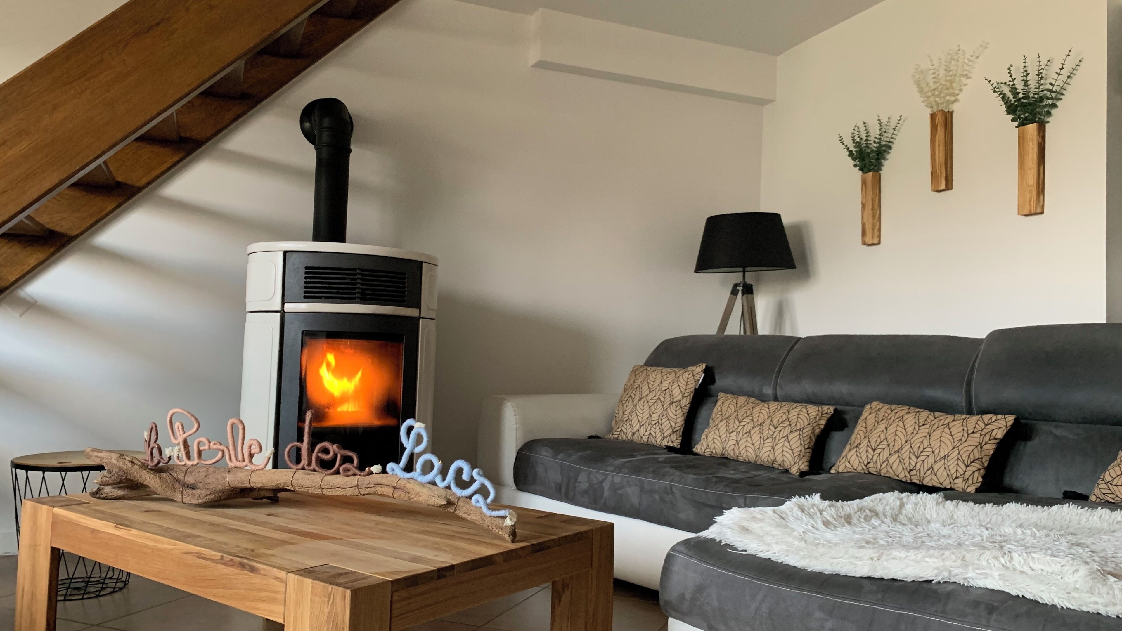 Un salon chaleureux avec un poêle à bois, un canapé gris foncé et une table basse en bois.