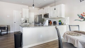 A modern kitchen with white cabinets, a stainless steel refrigerator, a microwave, and a sink. There is a dining area with a table and chairs. - 3 bedroom townhome in delightful Huntersville w AC, WiFi Near Birkdale Village (Huntersville)