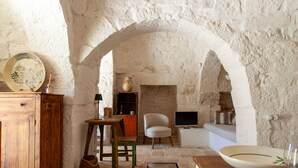Un intérieur rustique avec des murs en pierre, une table en bois, une chaise blanche et un bol posé sur un comptoir.