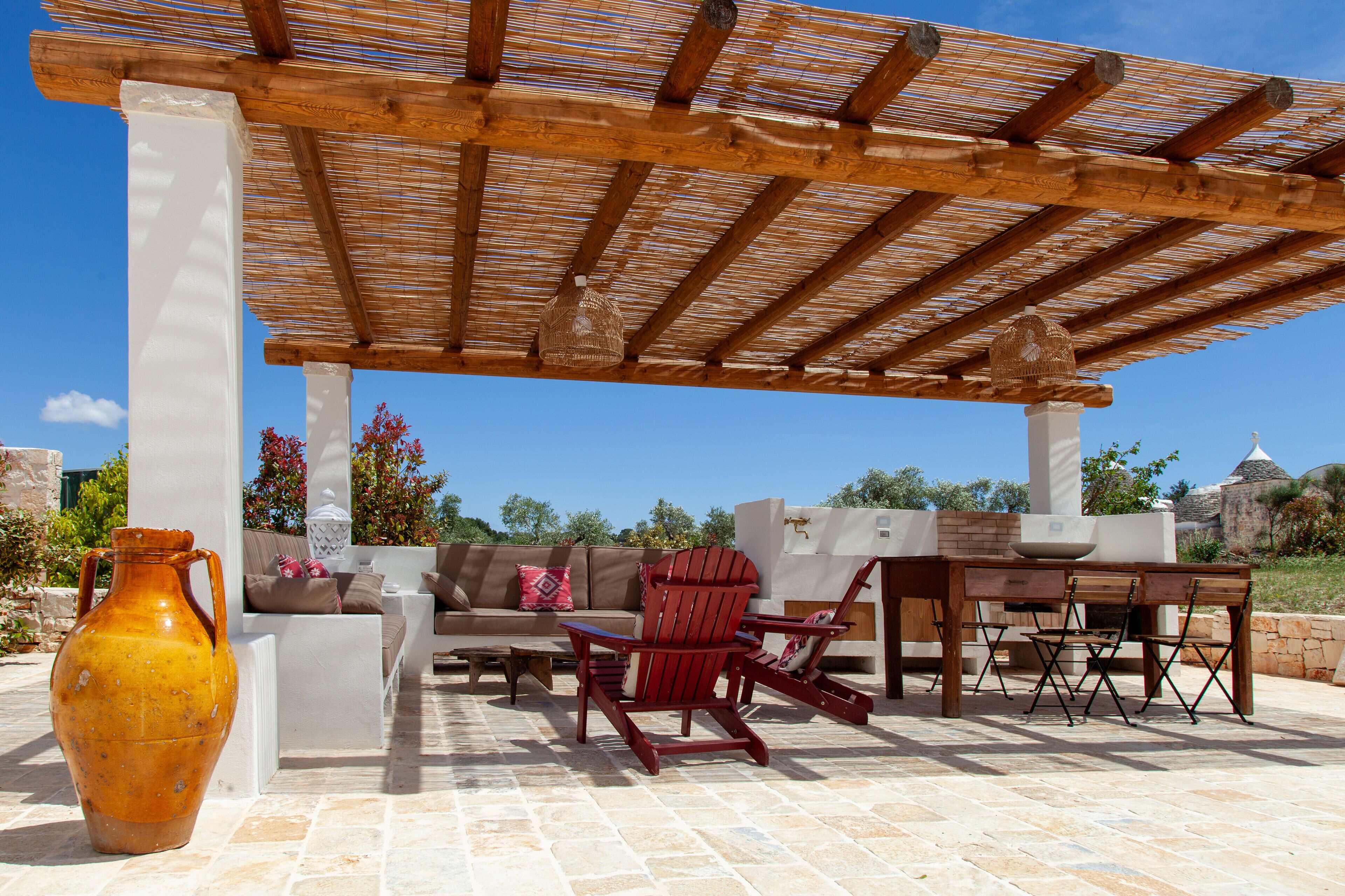 An outdoor patio with a wooden pergola, a sofa set, a dining table with chairs, and a large vase.