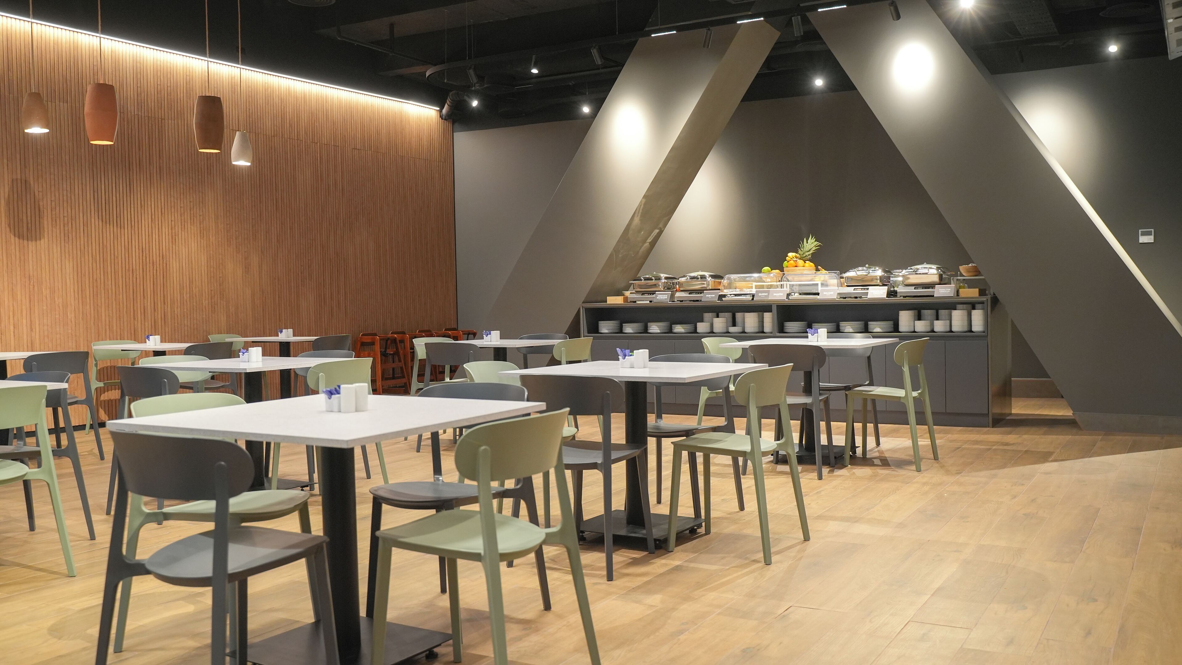 Un café moderne aux murs lambrés, offrant différents types de sièges, notamment des tables et des chaises, et doté d’un comptoir avec des distributeurs de nourriture et de boissons.