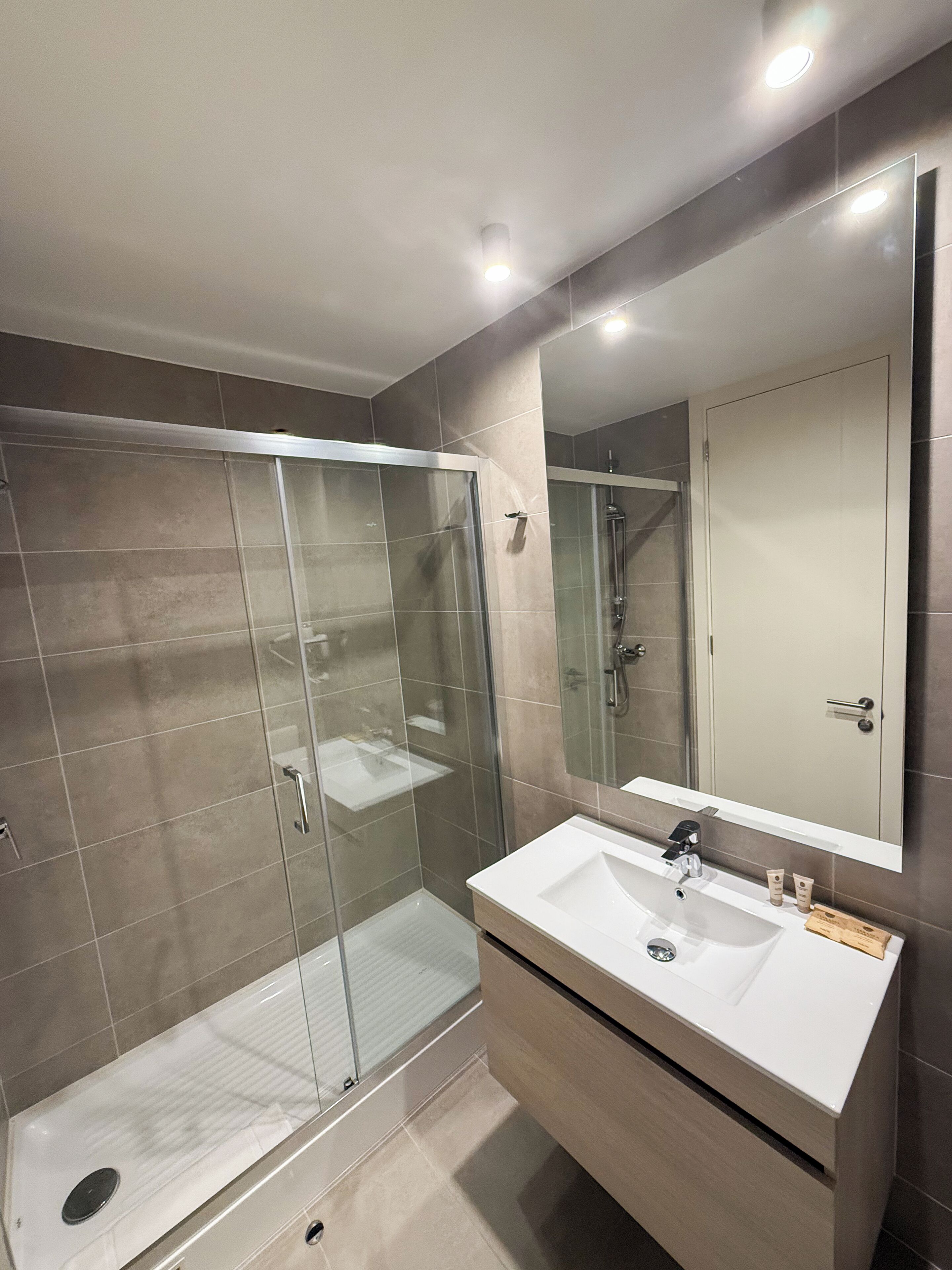Une salle de bain moderne avec une douche à parois de verre, un lavabo blanc et un grand miroir.