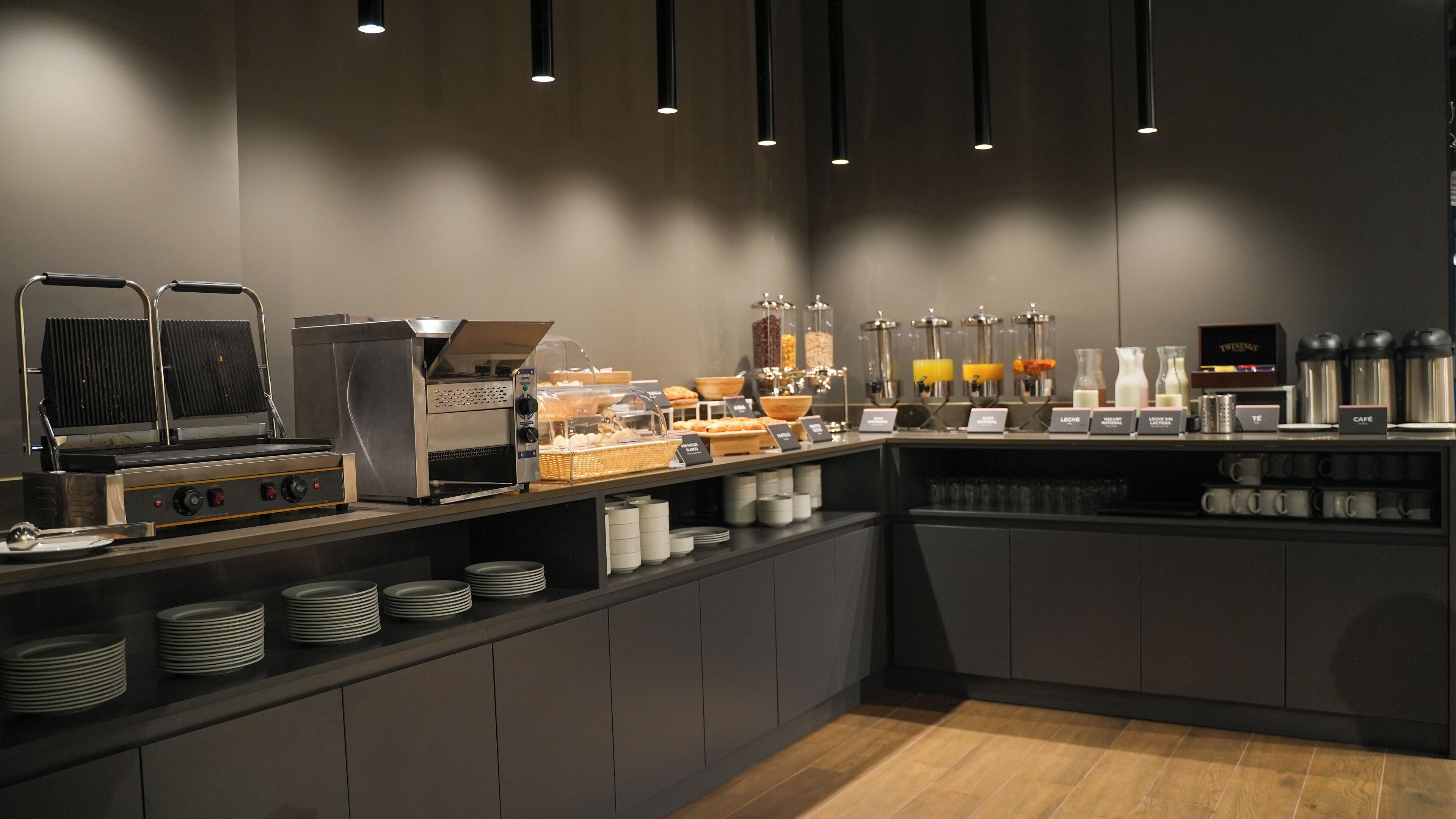 Een moderne ontbijtbar met een zelfbedieningsstation, inclusief een wafelijzer, koffieautomaten en diverse soorten etenswaren.