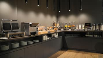 Een moderne ontbijtbar met een zelfbedieningsstation, inclusief een wafelijzer, koffieautomaten en diverse soorten etenswaren.