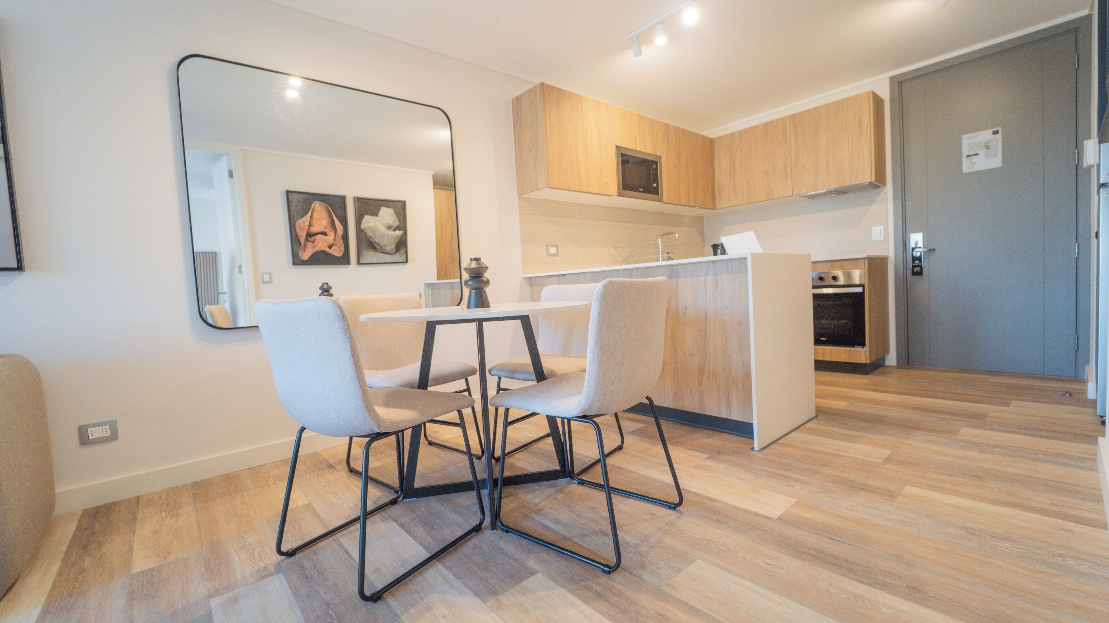 A modern kitchen with wooden cabinets, a built-in oven, and a dining area with a white table and chairs.