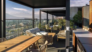 A modern outdoor terrace with wicker furniture, a wooden table, and a view of a cityscape and mountains. - Spot Suites (Santiago)