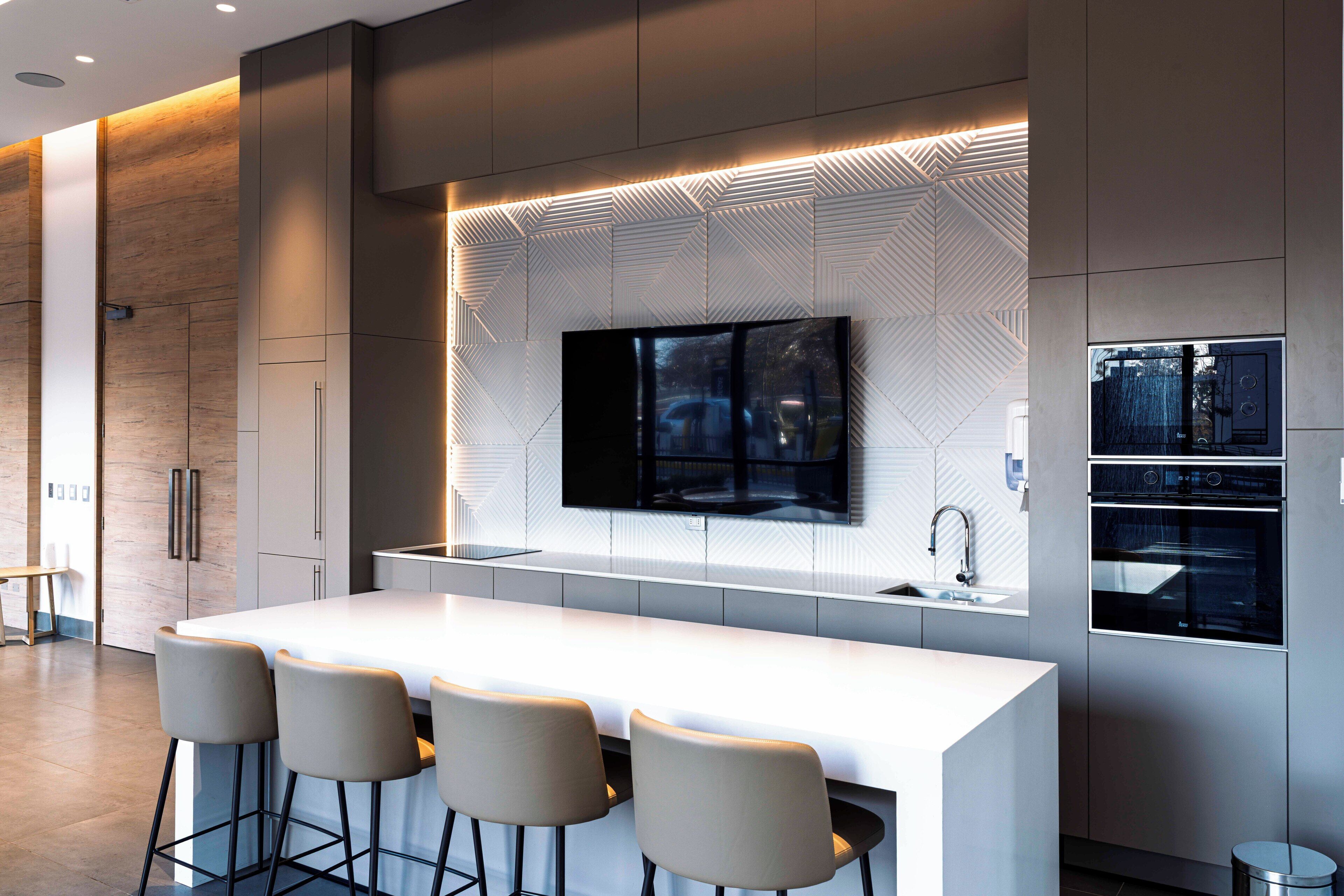 A modern kitchen with a central island, bar stools, a flat-screen TV, and built-in appliances.