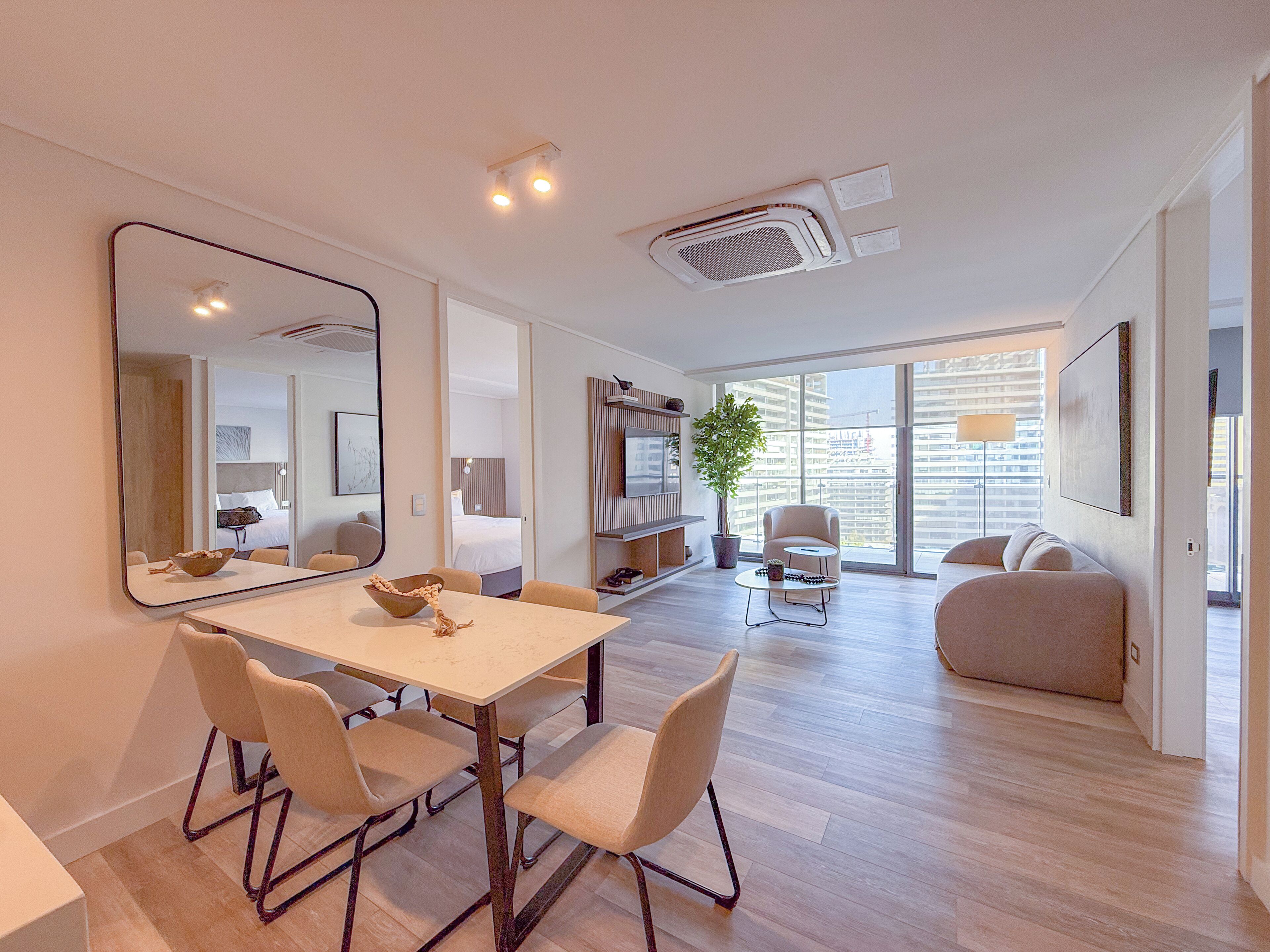 A modern living room with a dining area, large windows, a potted plant, and a sofa.