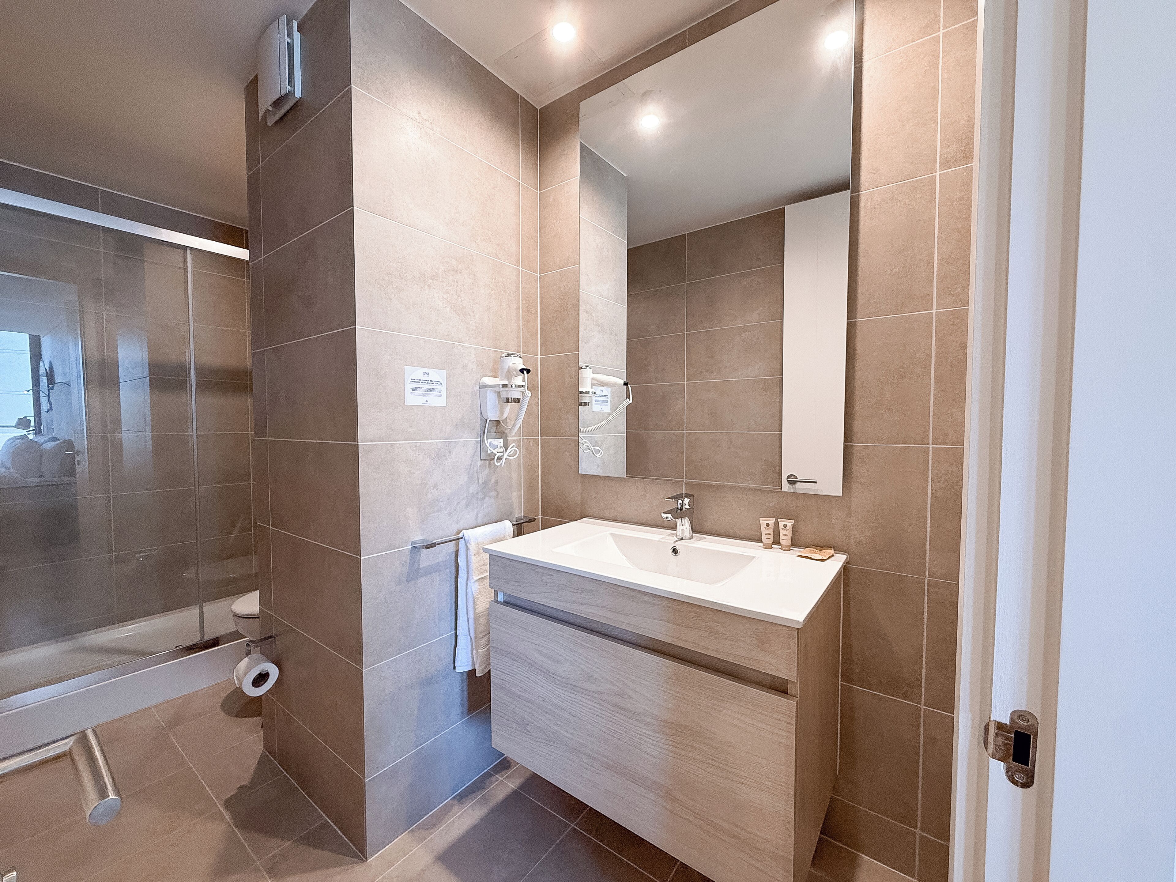 Une salle de bain moderne avec un grand miroir, un lavabo et un espace douche.