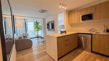 A modern kitchen with wooden cabinets, a stainless steel dishwasher, and a flat-screen TV mounted above the counter.