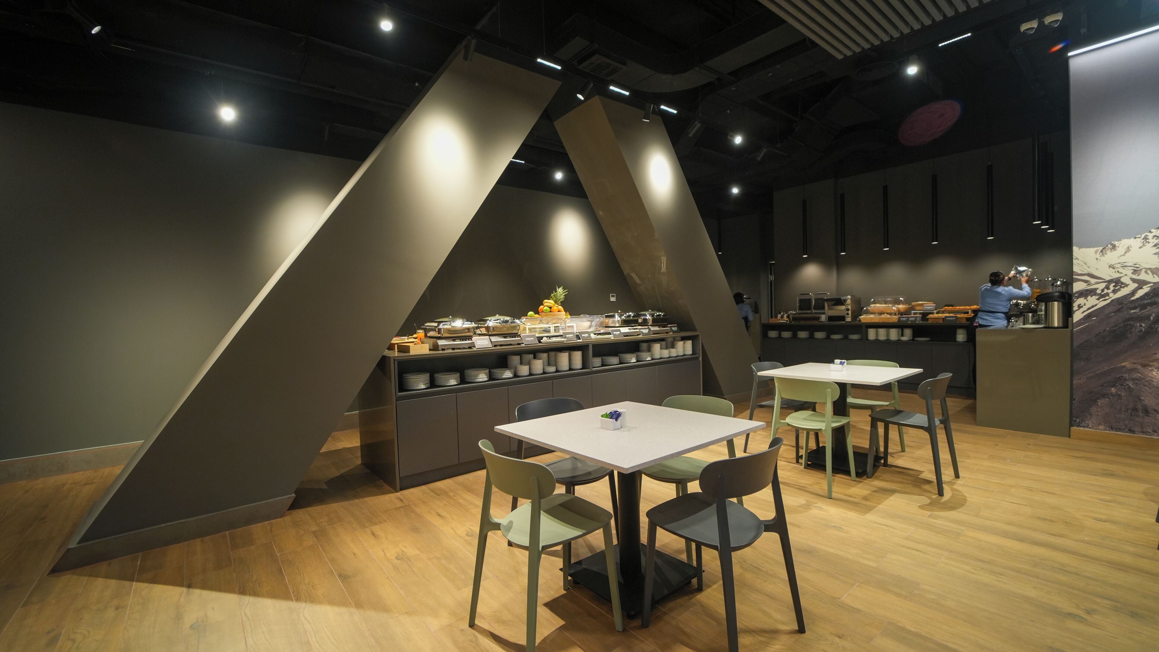 A modern cafe with a buffet counter, wooden flooring, and green chairs.