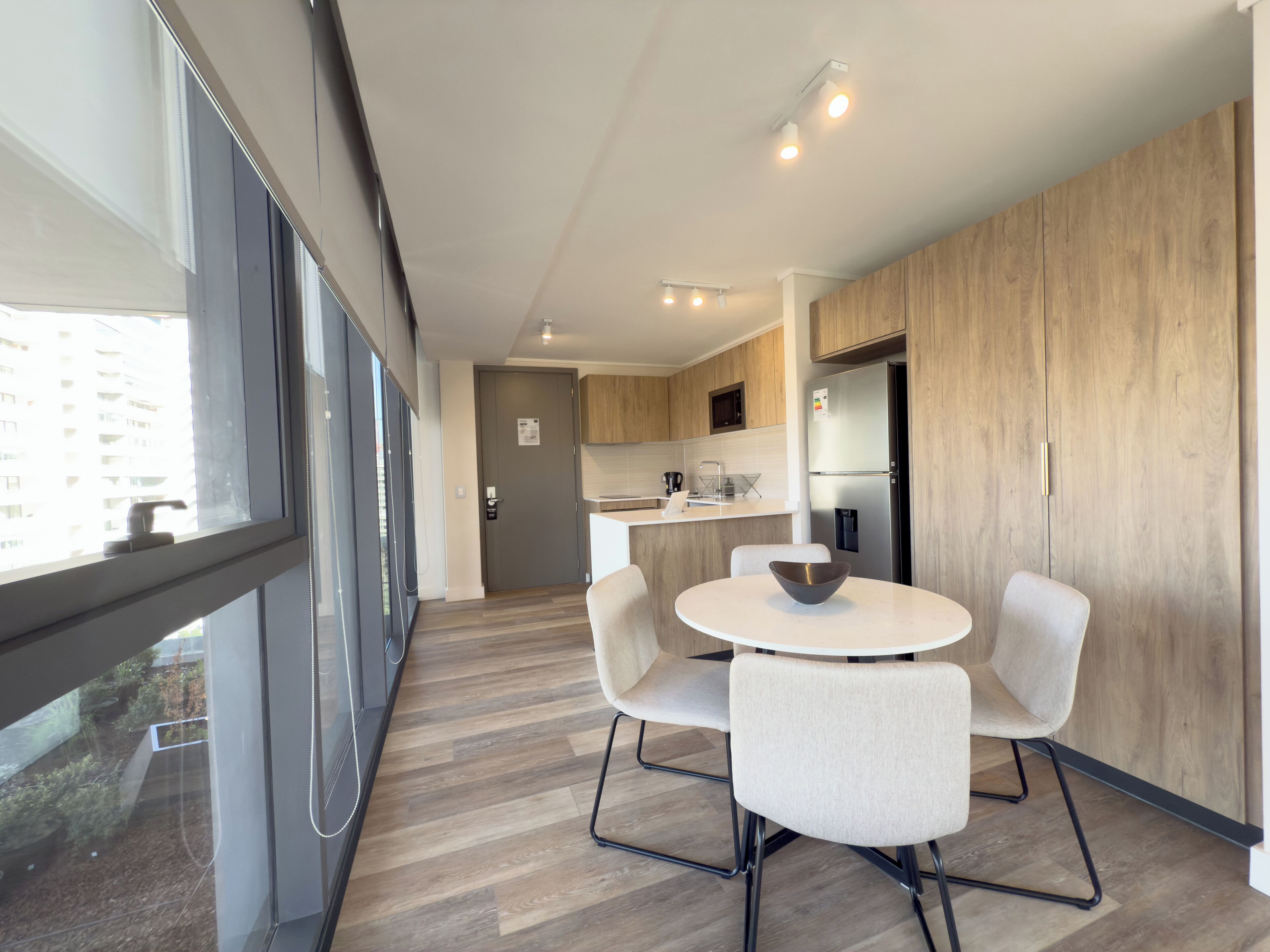 Une cuisine moderne avec un coin repas, de grandes fenêtres et une vue sur un bâtiment à l’extérieur.