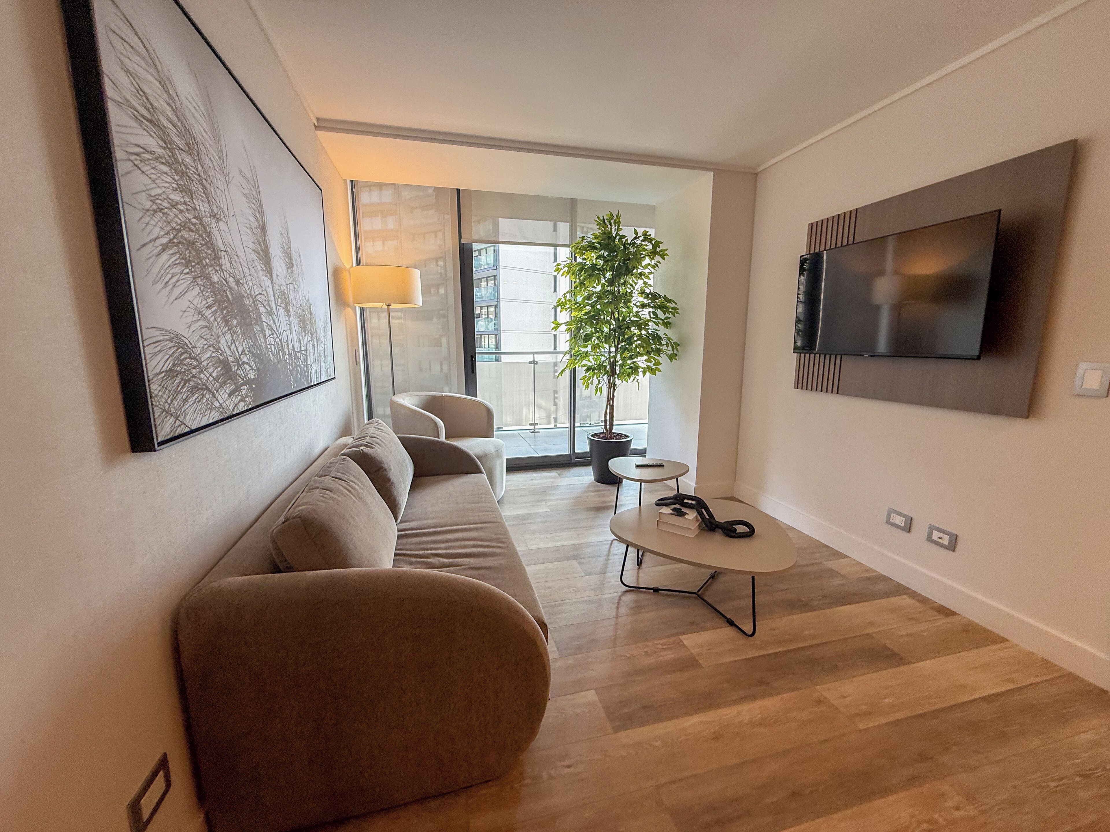 A modern living room with a sofa, a coffee table, a TV mounted on the wall, and a potted plant.