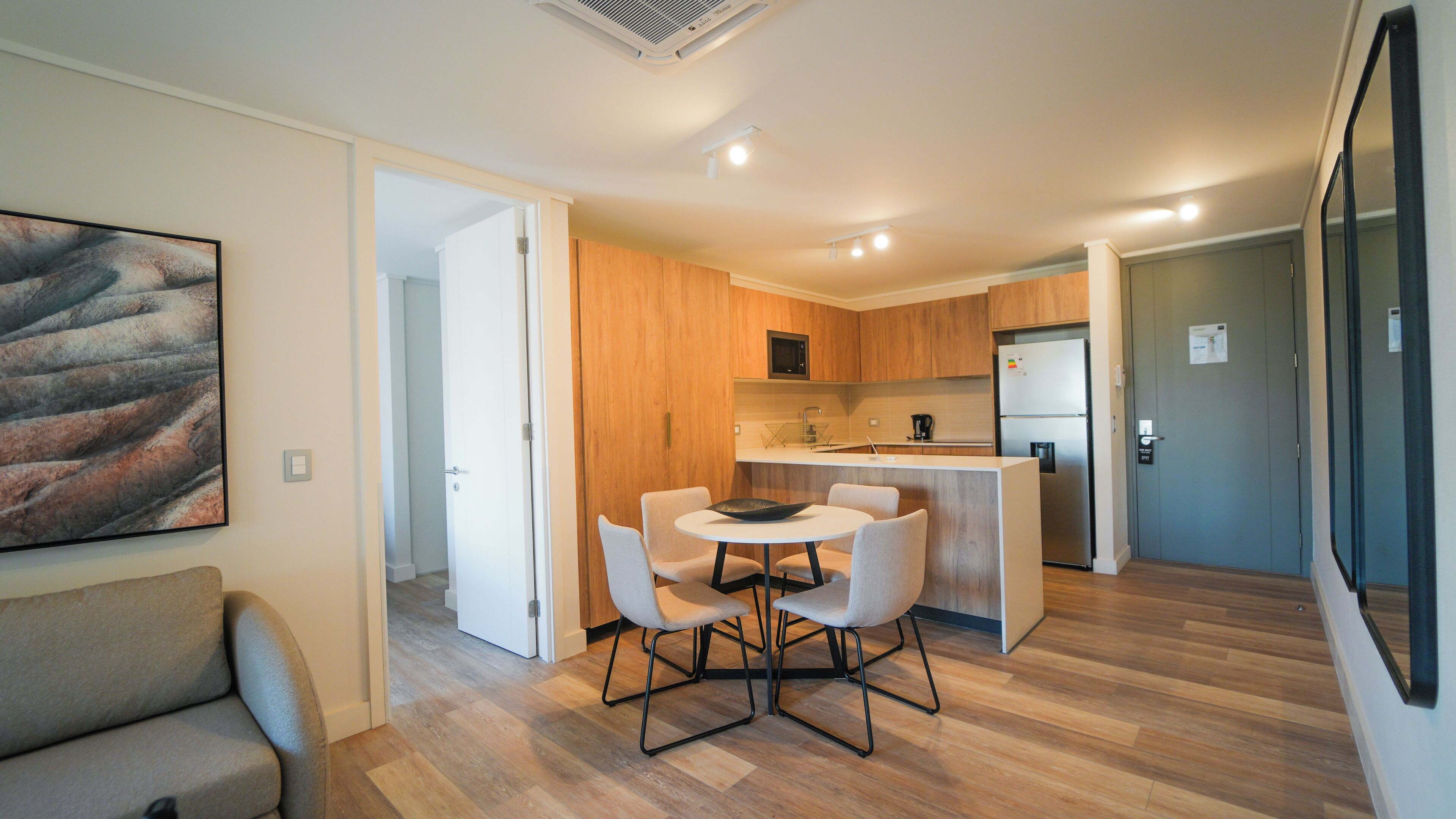 Una cocina moderna con armarios de madera, una isla central y un refrigerador. Hay un comedor con una mesa redonda y sillas.