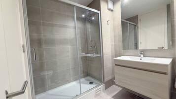A modern bathroom with a glass-enclosed shower, a sink with a mirror, and a vanity with drawers.