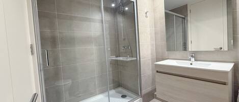 Un baño moderno con ducha de vidrio, lavamanos con espejo y tocador con cajones.