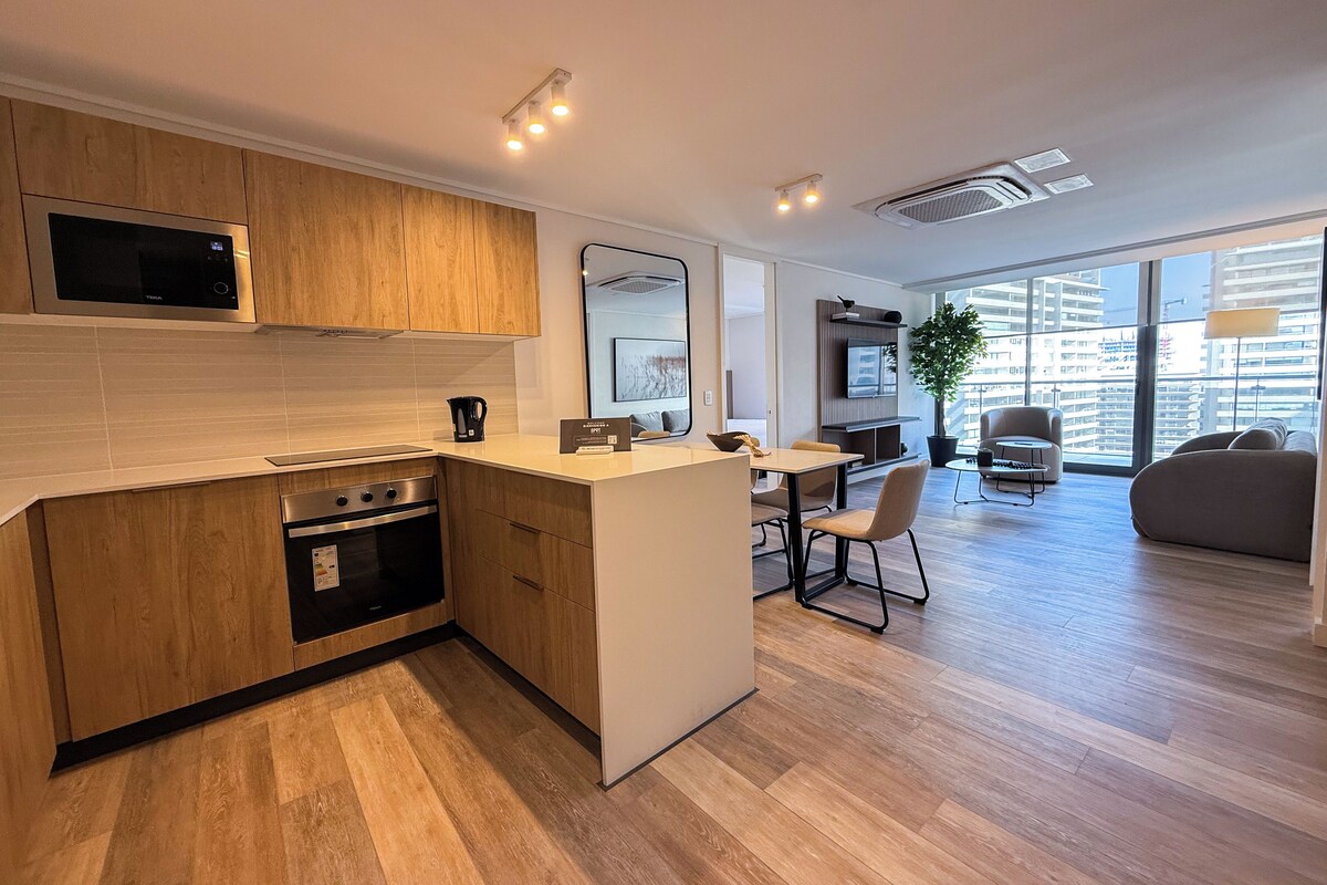 A modern kitchen with wooden cabinets, a built-in microwave, and a dining area with a table and chairs.