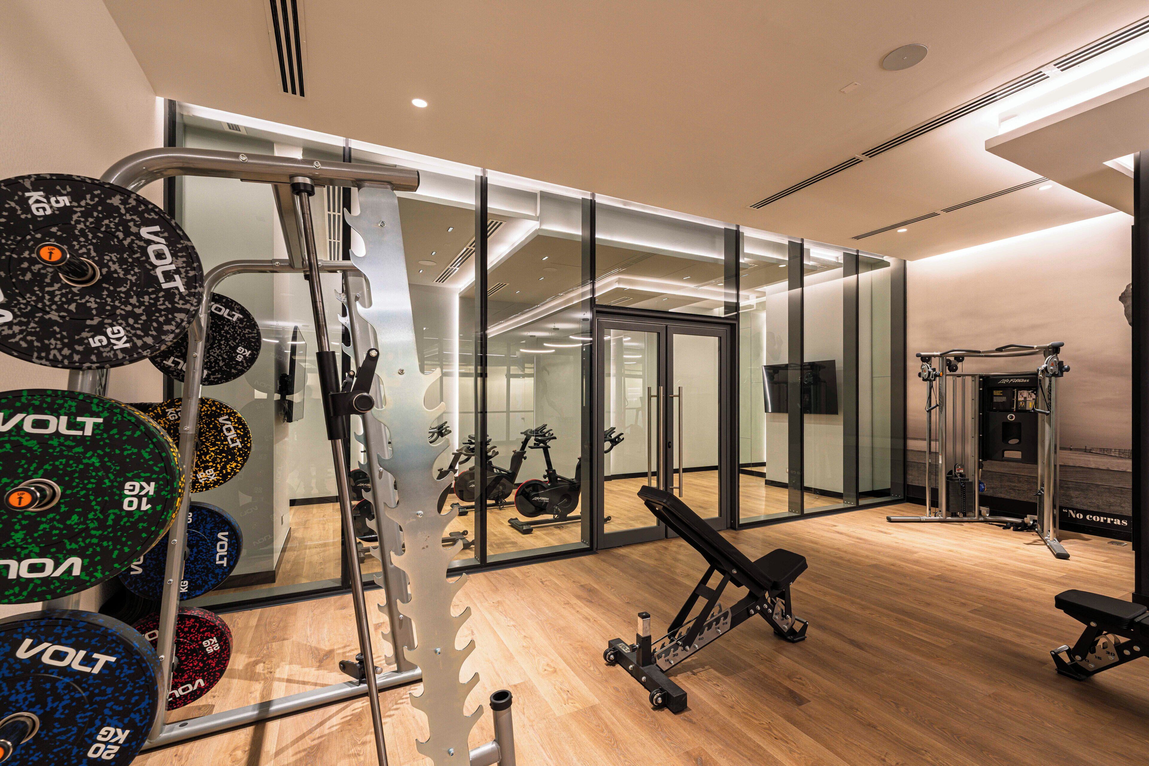 A modern gym with weightlifting equipment, exercise machines, and a wooden floor.