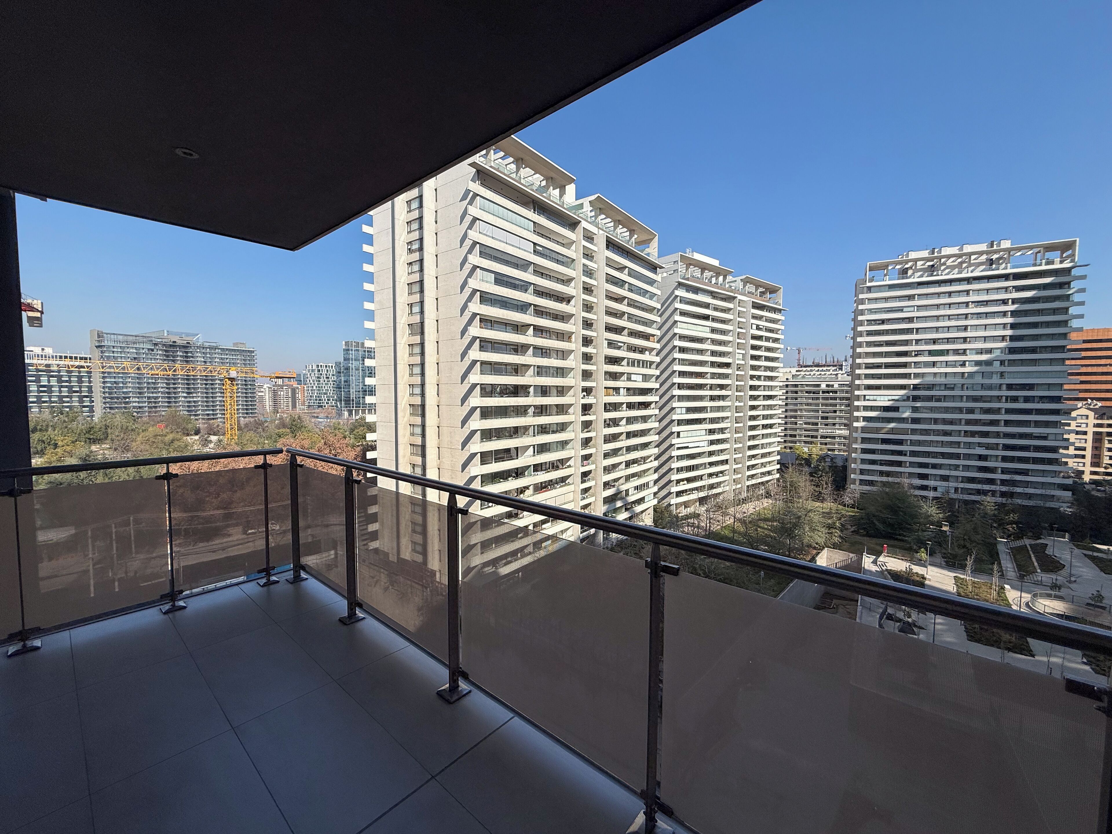 A balcony with a view of high-rise buildings, a construction crane, and a clear sky.
