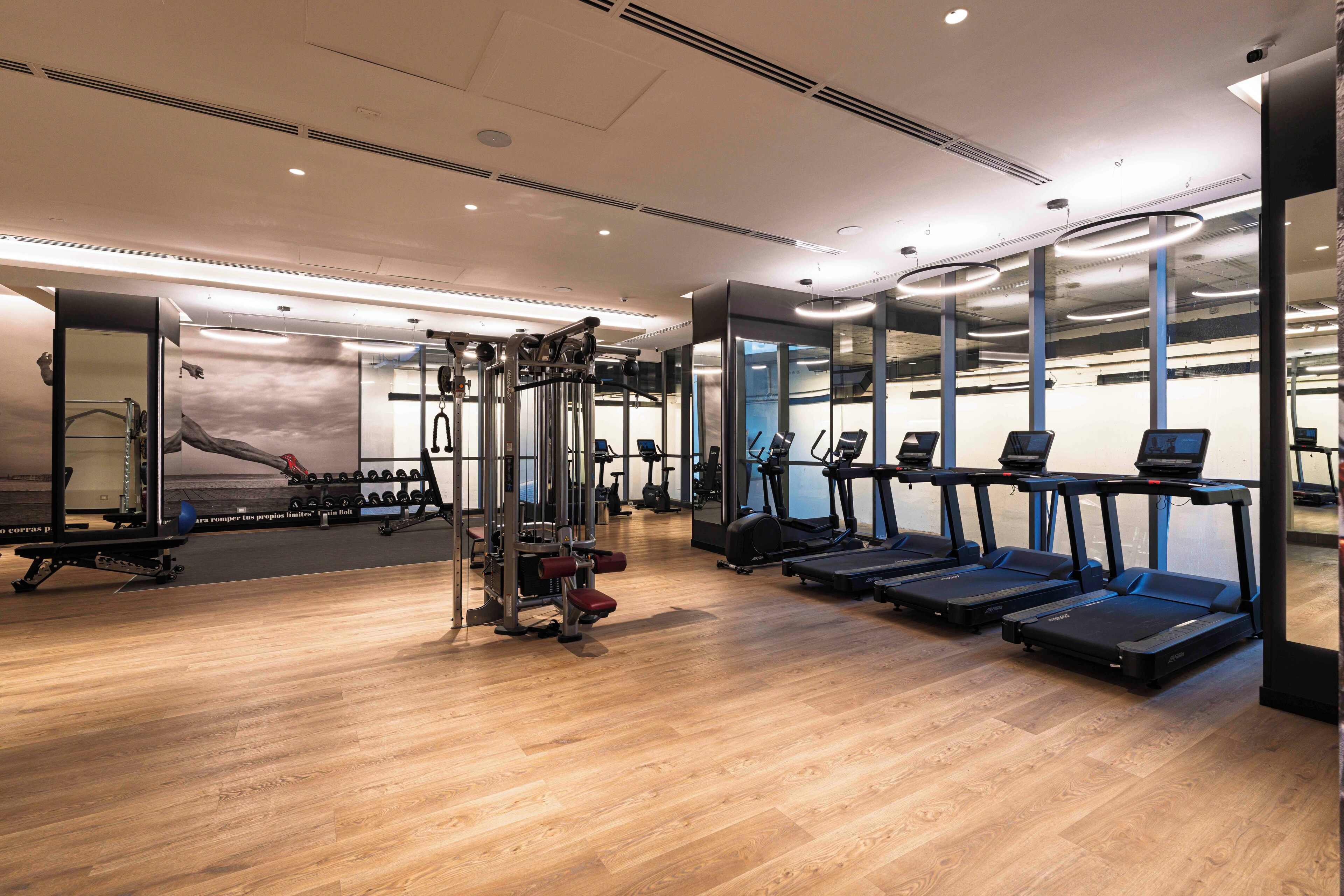 A modern gym with treadmills, weight machines, and a mirrored wall.