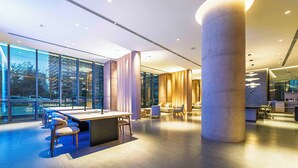 A modern hotel lobby with a large central column, seating areas, and large windows offering views of the city. - Spot Suites (Santiago)