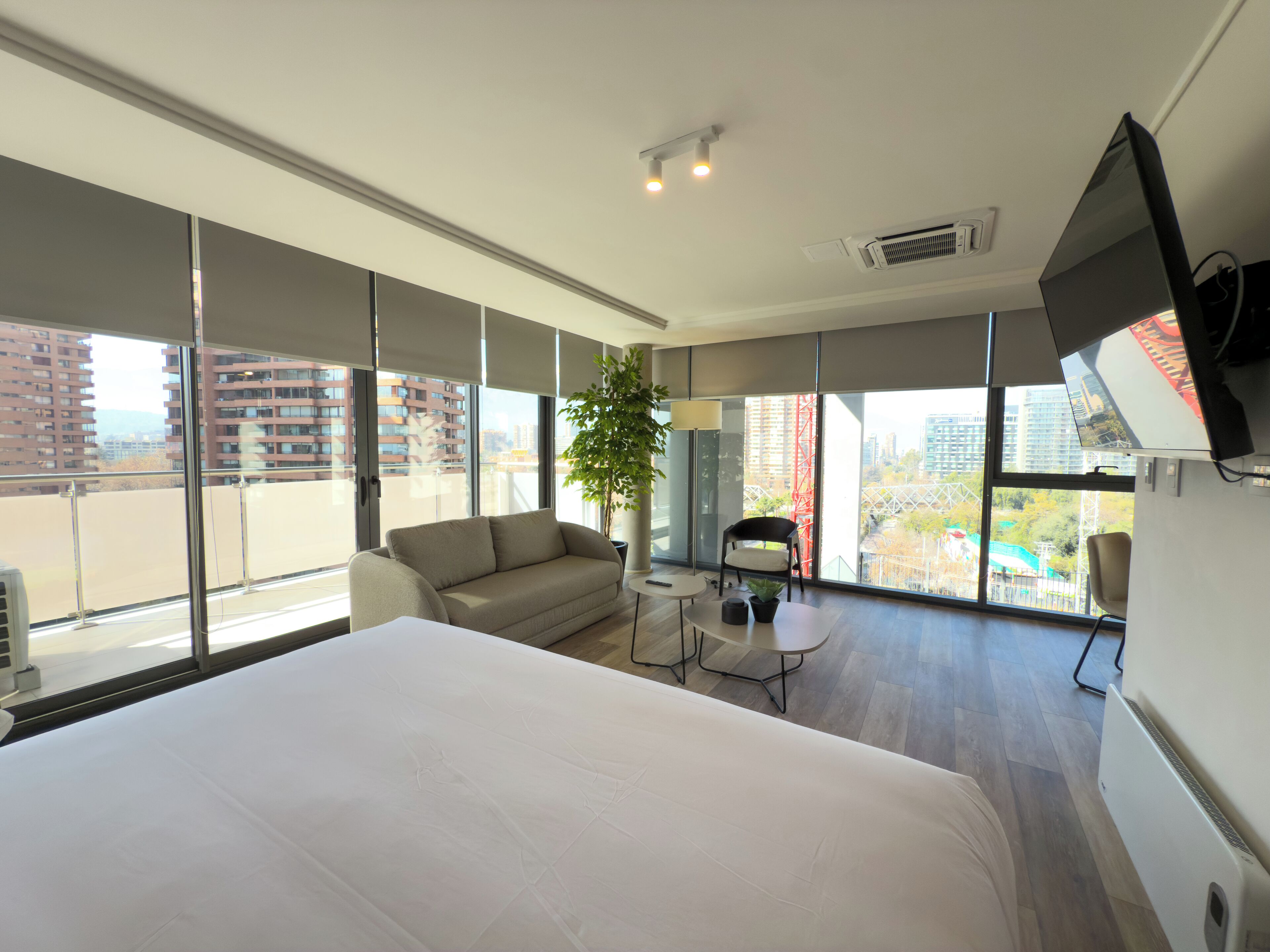 A modern hotel room with a large bed, a sofa, a small table, a chair, and a TV.