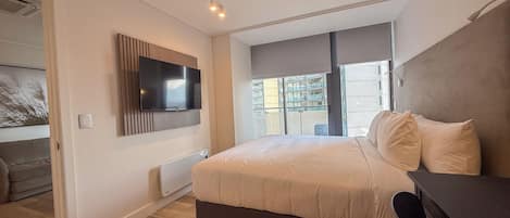 A modern bedroom with a large bed, a flat-screen TV mounted on the wall, and a view of the city through the window.