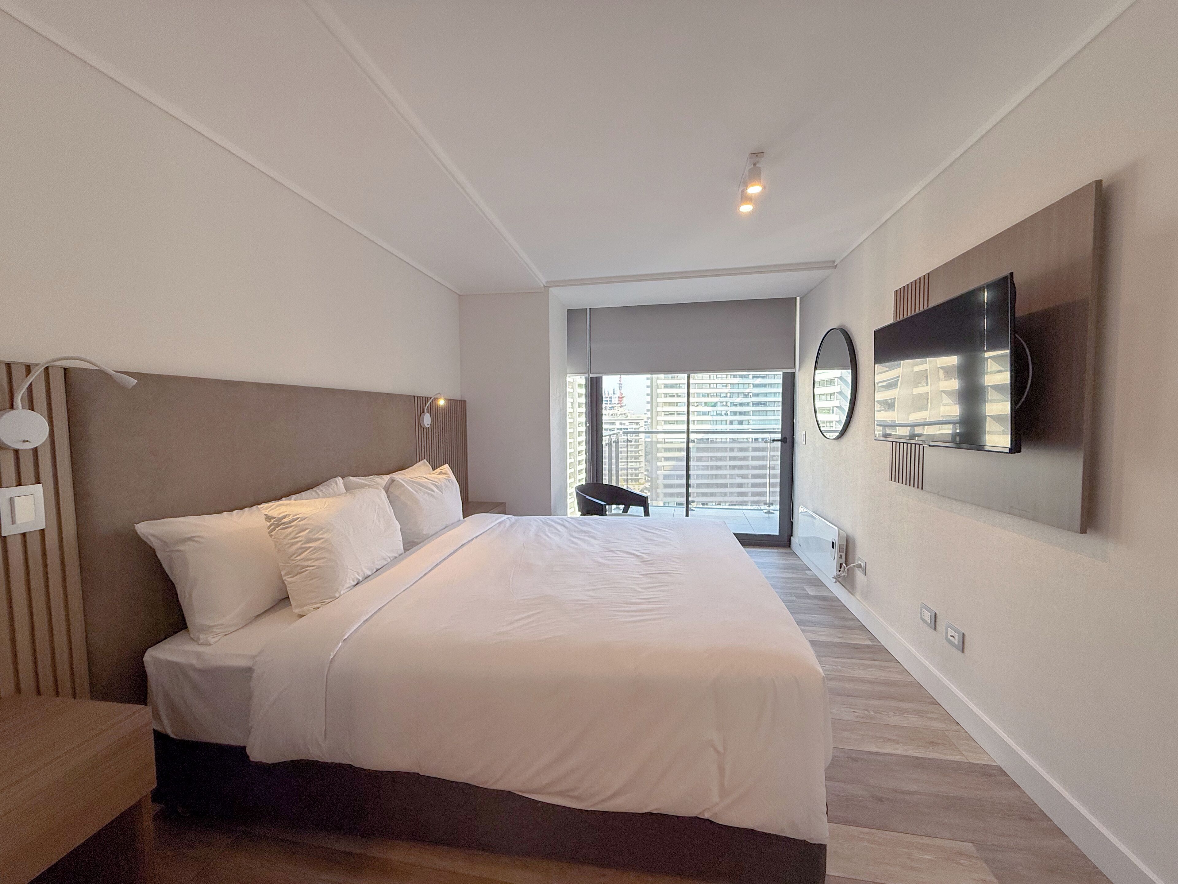 Une chambre moderne avec un grand lit, un téléviseur à écran plat fixé au mur et une vue sur la ville par la fenêtre.