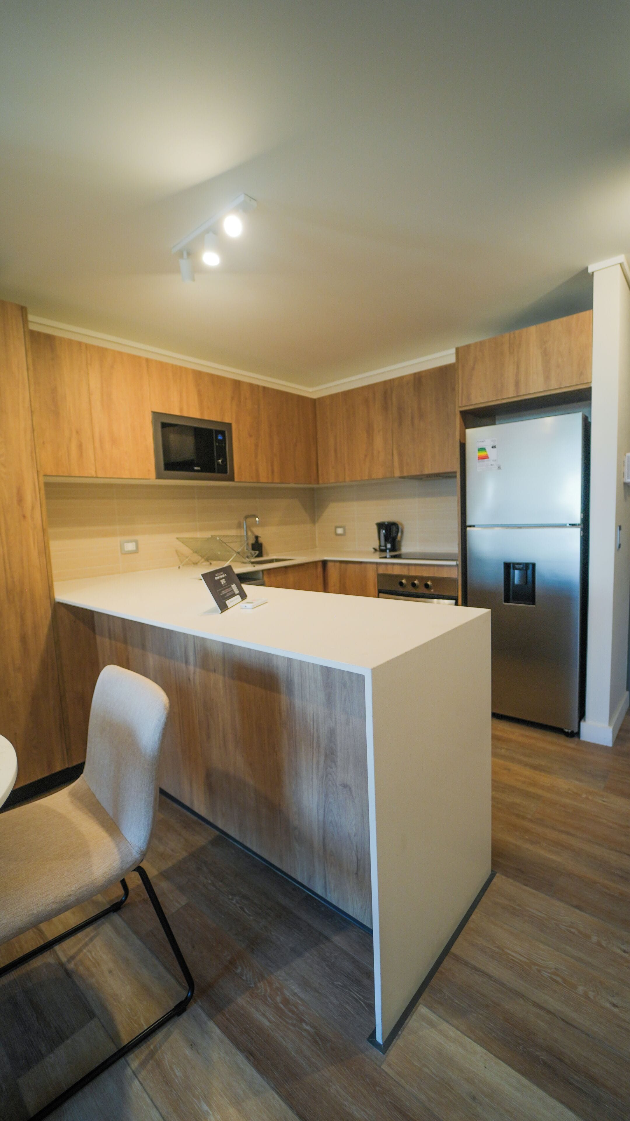 A modern kitchen with wooden cabinets, a stainless steel refrigerator, a microwave, and a coffee maker.