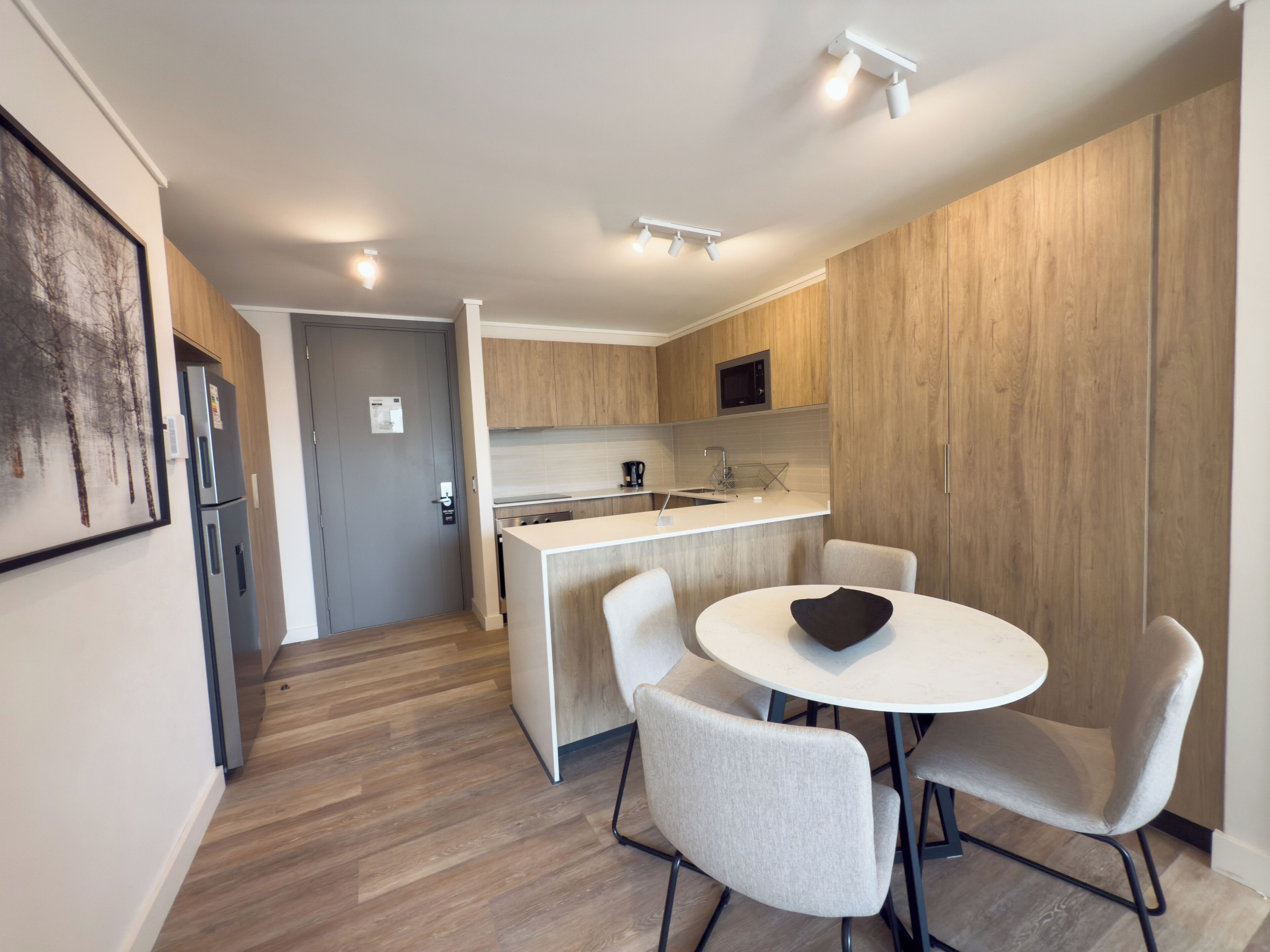 A modern kitchen with a dining area, featuring a built-in microwave, stainless steel appliances, and a white countertop.