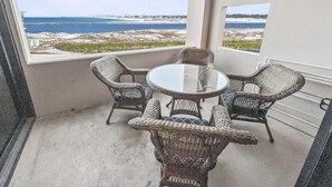 Un balcon doté de meubles en osier et d’une table en verre, offrant une vue sur la plage.