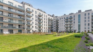 A modern apartment building with multiple balconies, a grassy courtyard, and a pathway lined with flowers. - Lion Apartments - Angielska Grobla II (Gdansk)