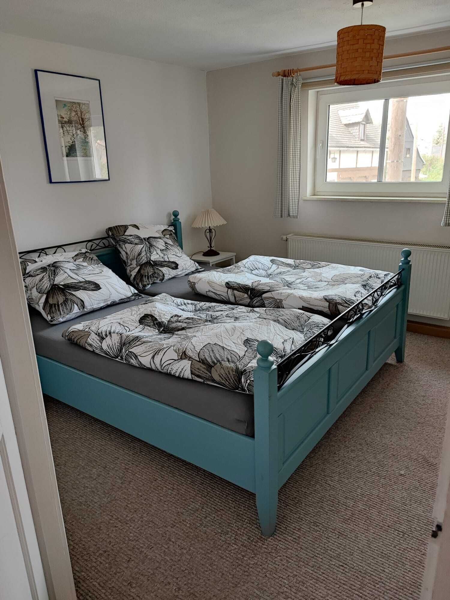 Un dormitorio con cama, mesita de noche, lámpara, ventana con cortinas y una lámpara colgante.