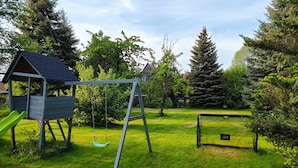 Un parque infantil con columpios y tobogán, rodeado de exuberante follaje y árboles.