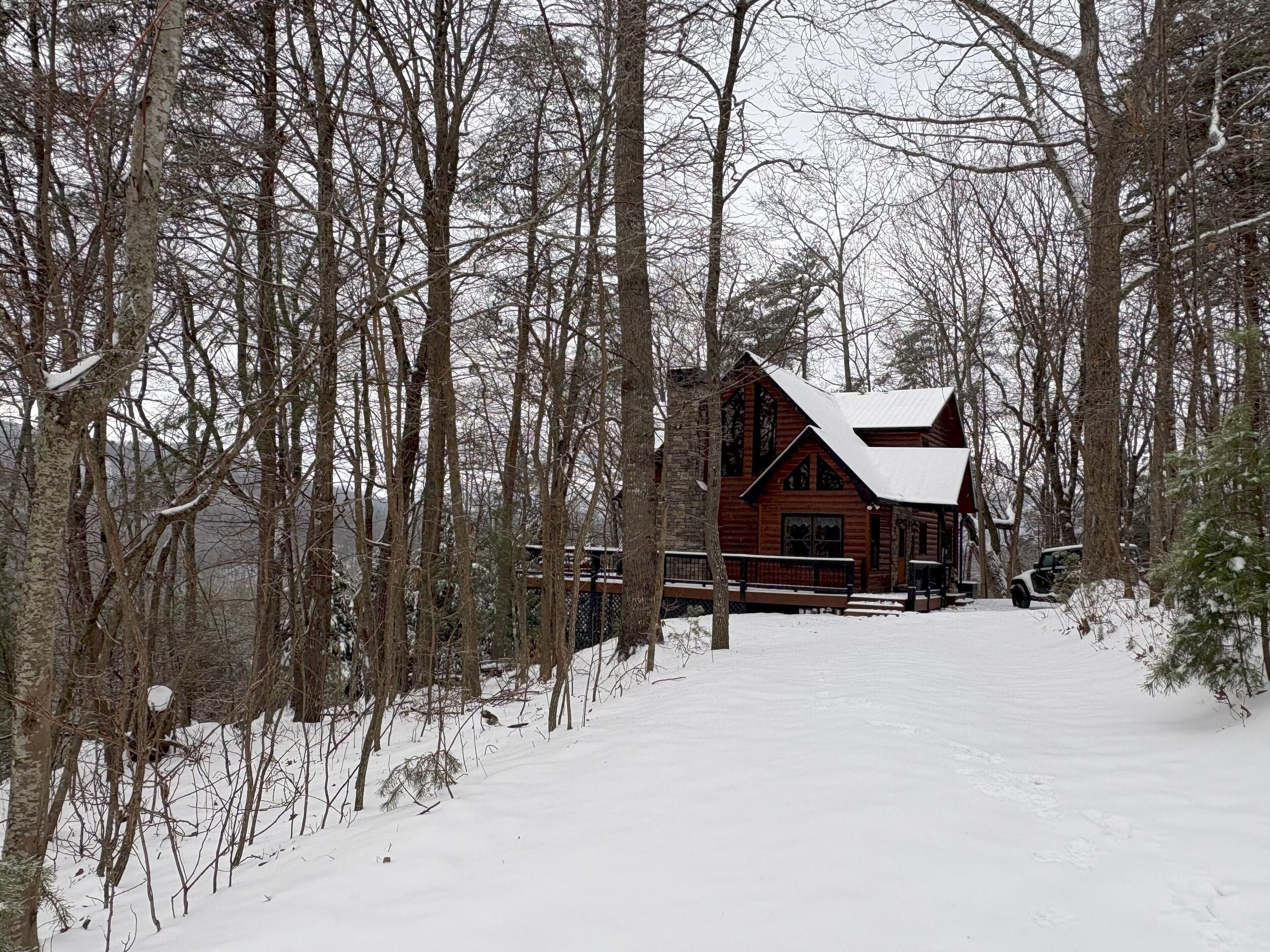 Una cabaña de troncos con tejado nevado, rodeada por un bosque.