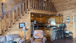 A wooden cabin interior with a staircase, kitchen, dining area, and a living room with a dog. - BLUE RIDGE SPLENDOR - 3 BR, 3 BA amazing cabin, with incredible mountain views! (Cherry Log)