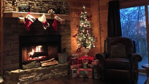 A cozy cabin interior with a stone fireplace, a Christmas tree, and a leather armchair. - BLUE RIDGE SPLENDOR - 3 BR, 3 BA amazing cabin, with incredible mountain views! (Cherry Log)