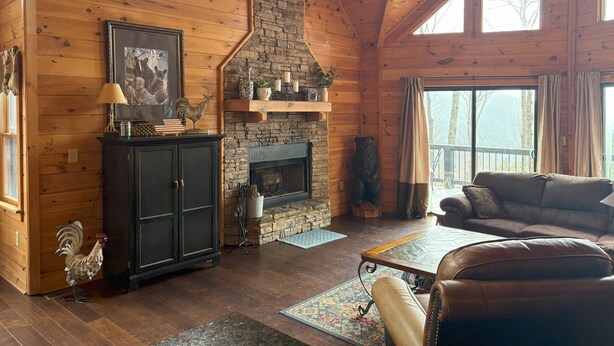 A log cabin interior with a fireplace, wooden walls, a leather sofa, and a dining table. - BLUE RIDGE SPLENDOR - 3 BR, 3 BA amazing cabin, with incredible mountain views! (Cherry Log)