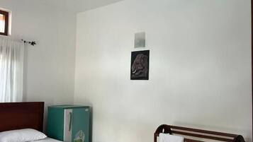 Una habitación de hotel con una cama, ventilador de techo, un pequeño armario y un perchero.