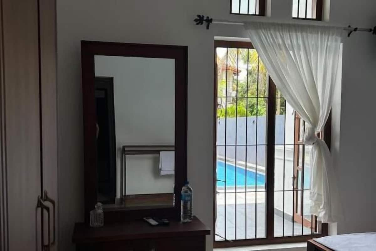 Quarto com cômoda de madeira, espelho, janela com vista para piscina e cortina.