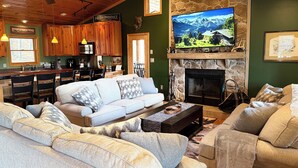 Ein gemütliches Wohnzimmer mit Kamin, einem großen Fernseher und einer Küche im Hintergrund.