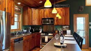 Eine Küche mit Holzausstattung, Edelstahlgeräten und einer Kochinsel, auf der ein Weinglas und eine Weinflasche stehen.