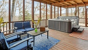 Eine überdachte Holzterrasse mit Blick auf Bäume und Berge, ausgestattet mit einem Whirlpool und blauen, gepolsterten Sitzmöbeln.