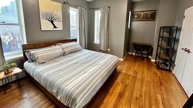 A bedroom with a large bed, a nightstand, a window with curtains, a wall-mounted shelf, and a door.