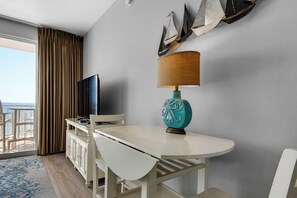 Habitació d'hotel amb balcó, televisió, taula i cadires, i una làmpada decorativa.