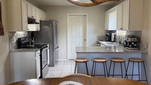 Una cocina moderna con armarios blancos, un refrigerador de acero inoxidable, horno empotrado y una zona de bar con taburetes.
