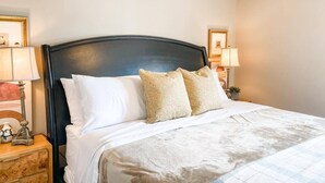 Una cama bien hecha con almohadas blancas y estampadas, un cabecero oscuro y lámparas de noche.