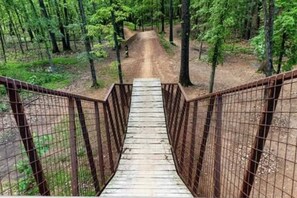 A wooden bridge with metal railings leading into a forested area. - Dwtn Bentonville Bike Retreat Hot Tub+MTB Trails (Bentonville)