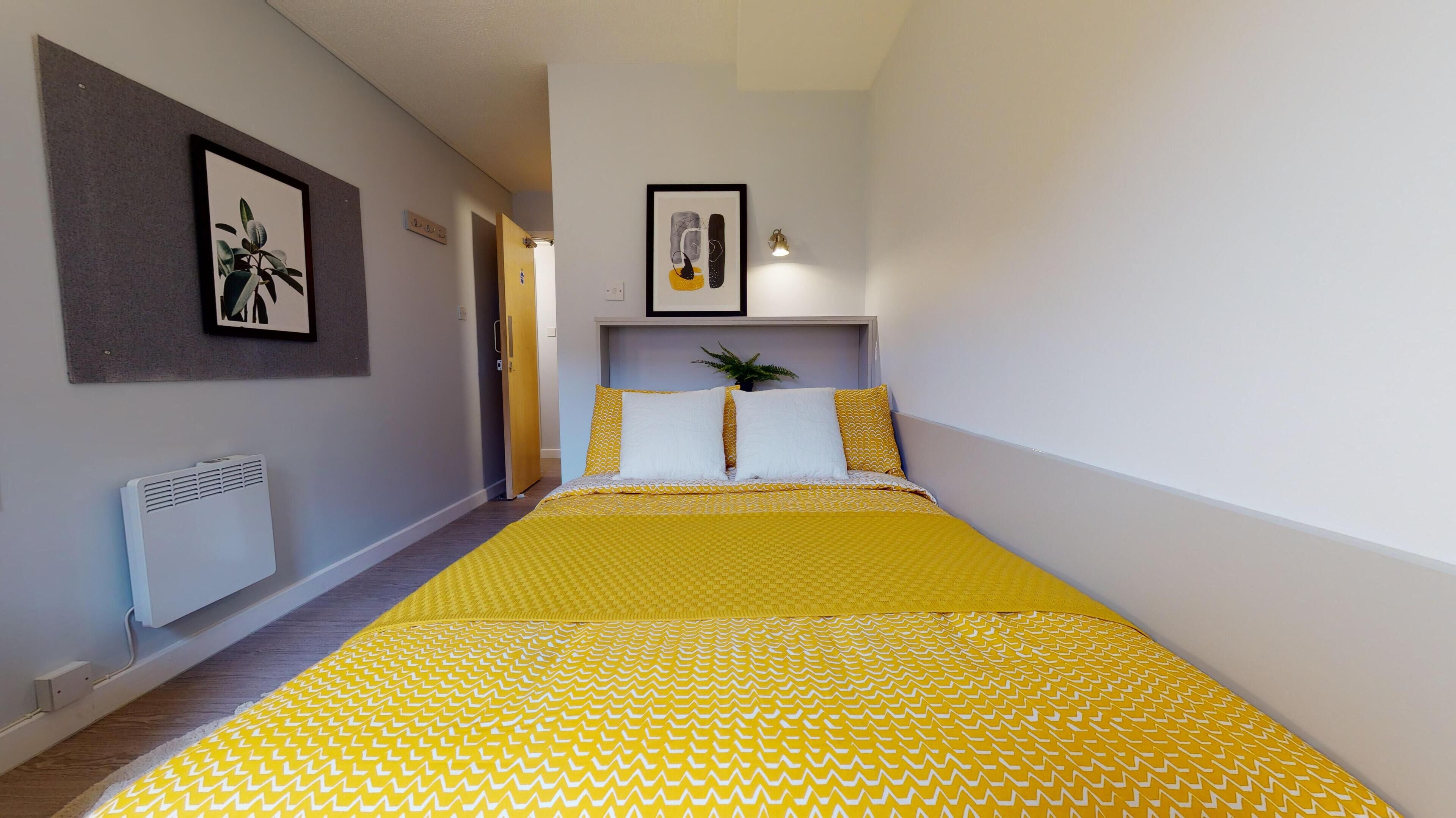 A bedroom with a bed, a radiator, a door, and a wall-mounted light fixture.